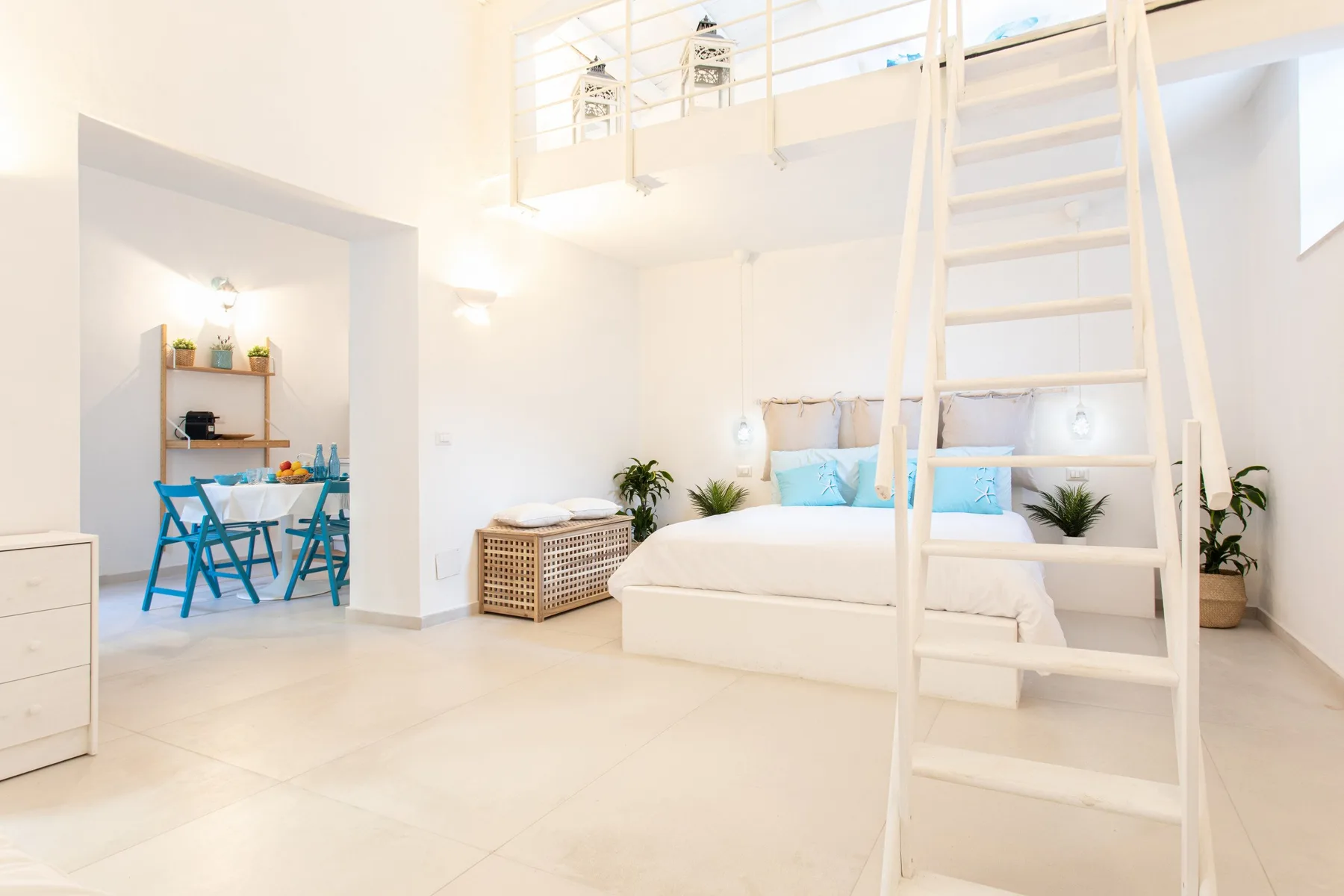 A bright bedroom with a raised sleeping area, ladder, and dining nook.