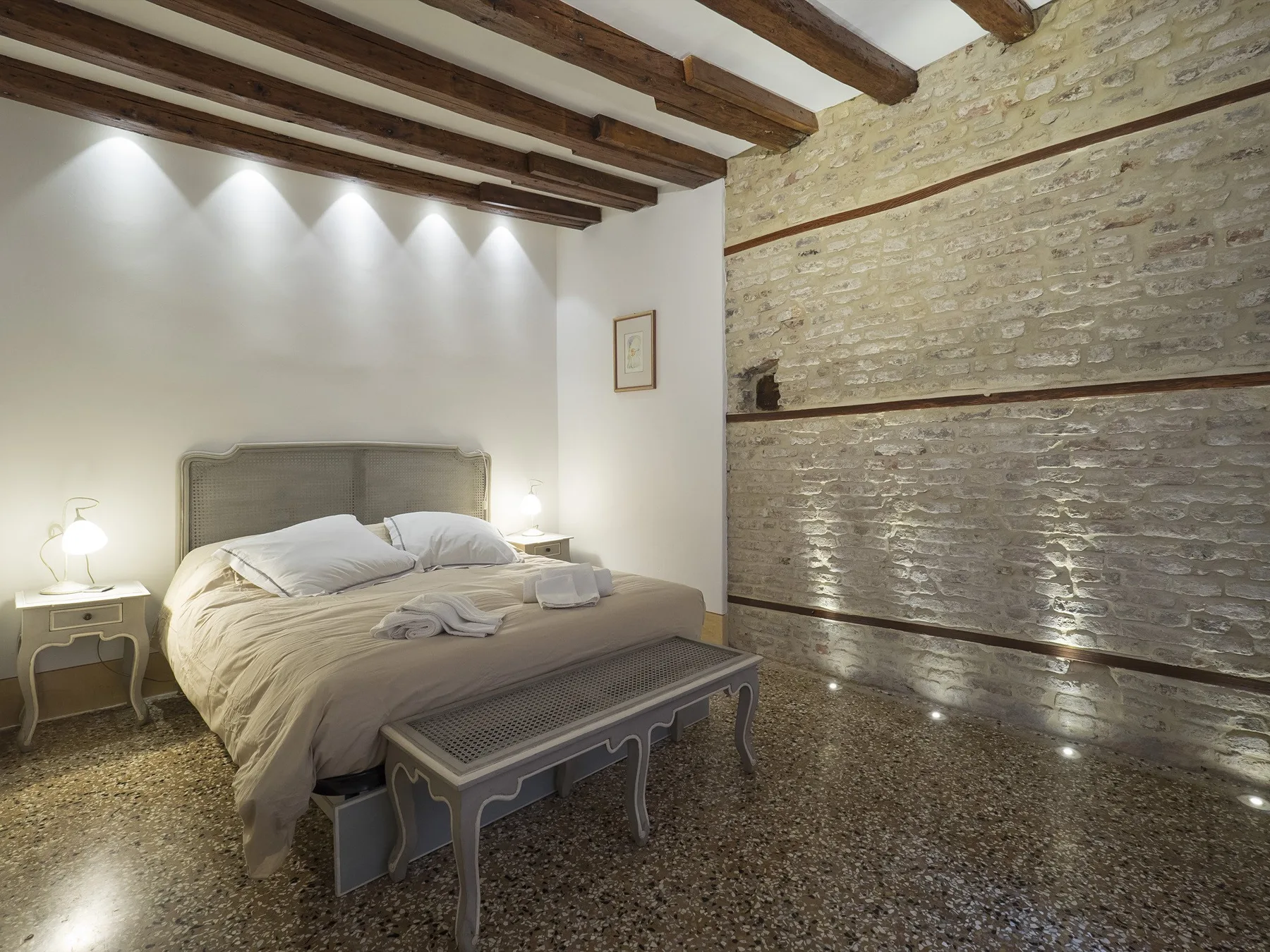Un dormitorio con una cama, un banco y vigas expuestas en el techo.