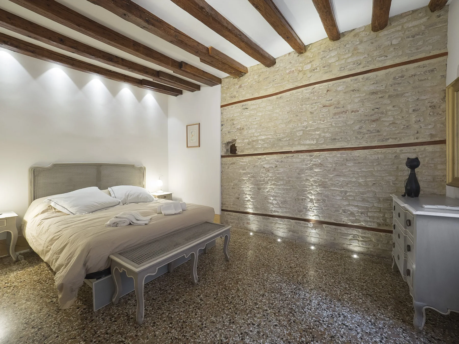 Un dormitorio con una cama junto a una pared de piedra y vigas de madera vistas en el techo.