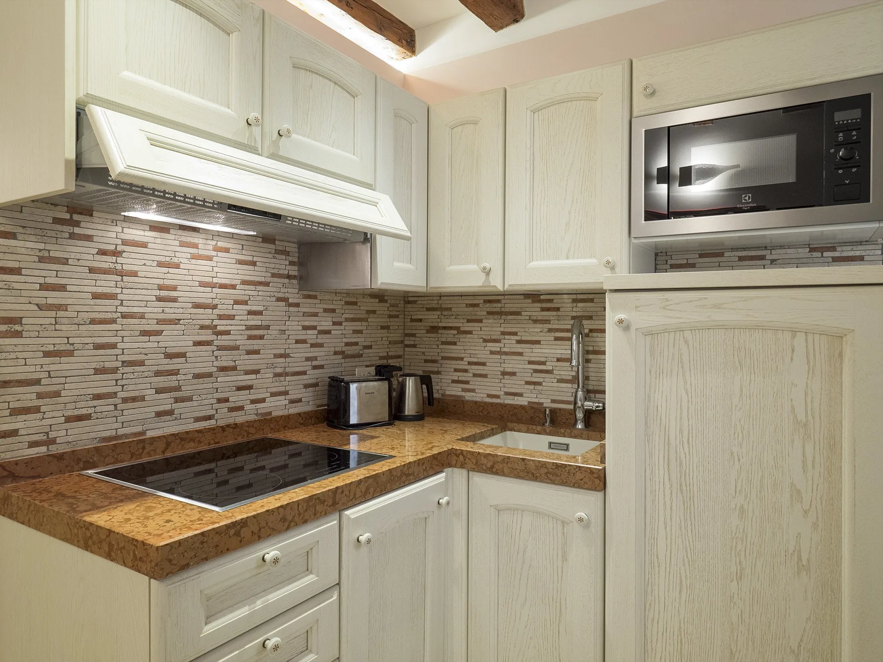 Una cocina compacta con gabinetes claros, una placa de cocción oscura y un salpicadero de azulejos.