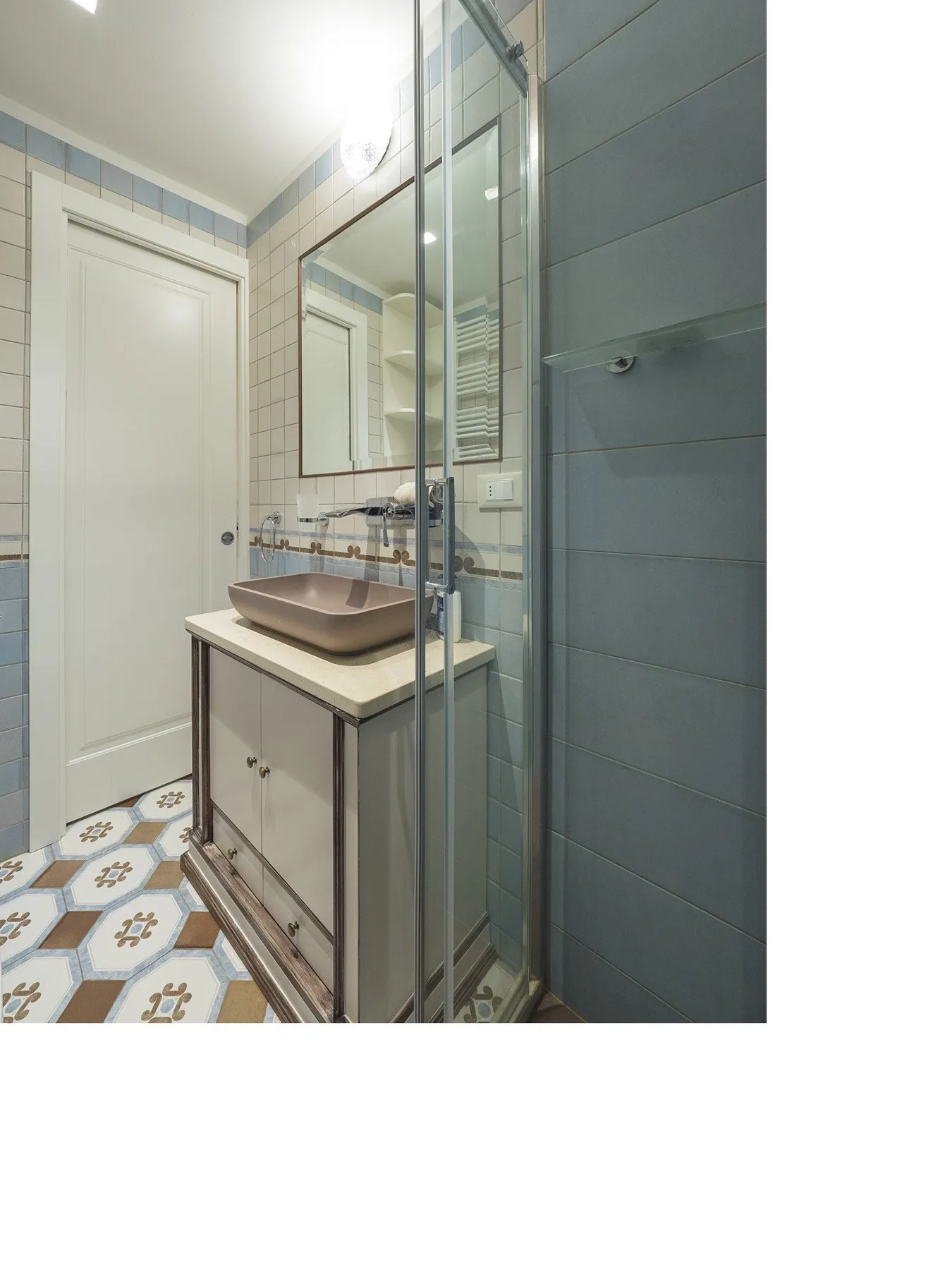 Baño alicatado con lavabo sobre mueble y ducha de vidrio.