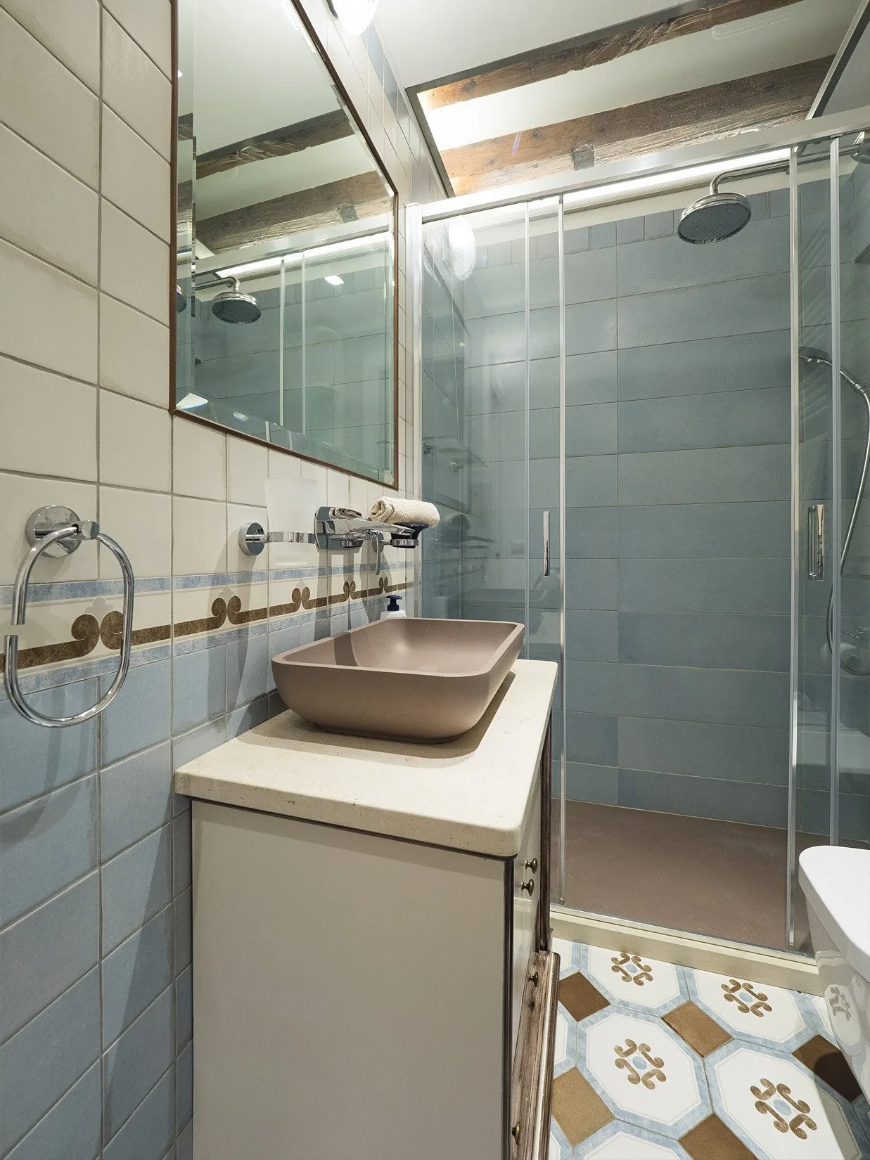 Un baño revestido de azulejos con lavabo, espejo y ducha de vidrio.
