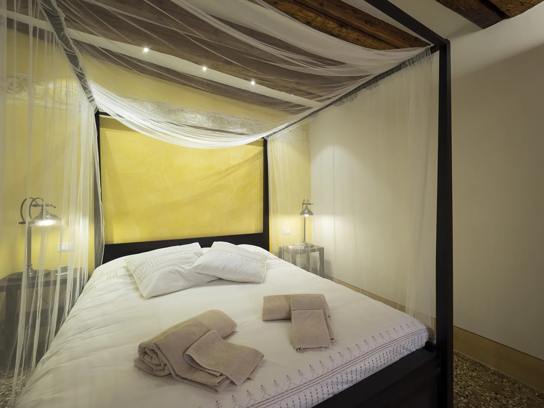 Un dormitorio con una cama vestida de blanco bajo un dosel de tela.