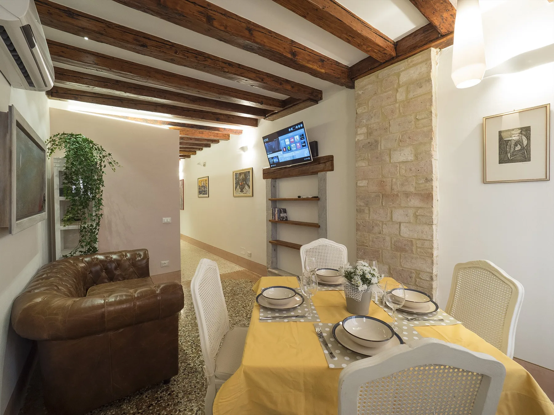 Comedor con la mesa puesta junto a un sofá de cuero y vigas de techo a la vista.