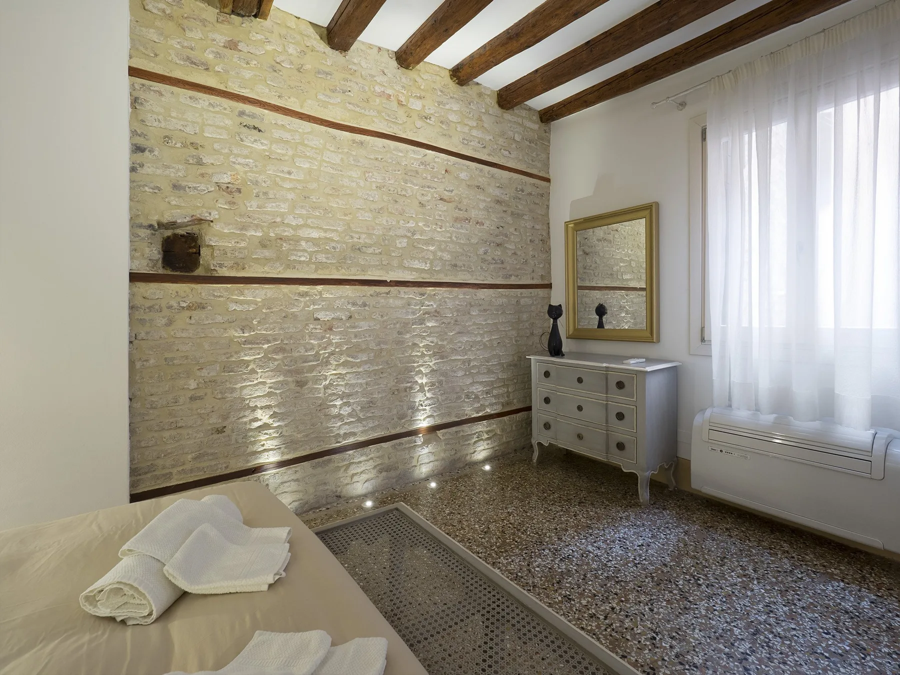 Un dormitorio con vigas vistas, una pared de piedra y una cama junto al borde.