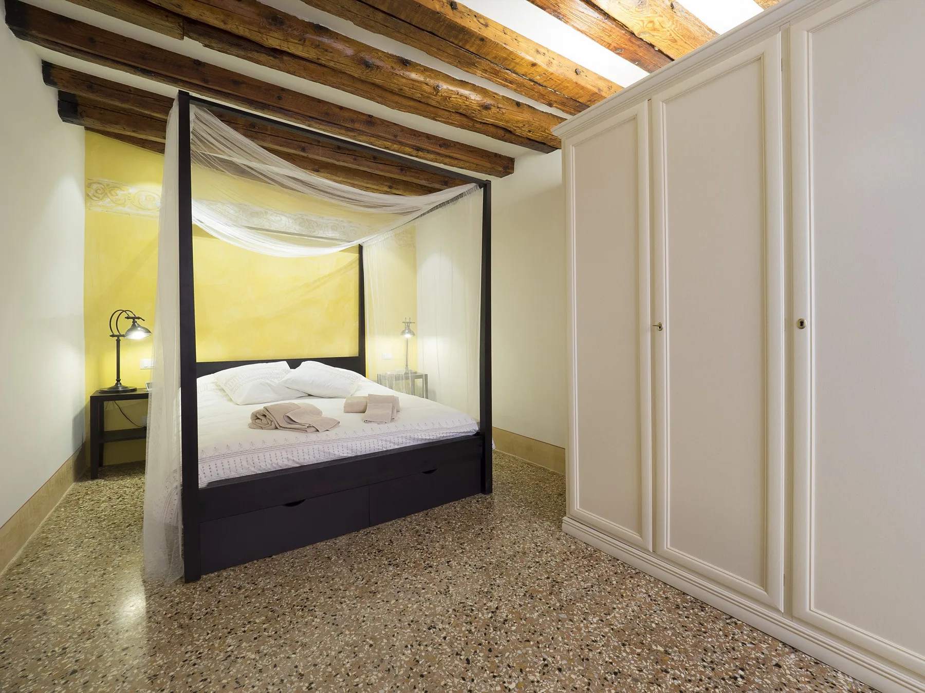 Un dormitorio con una cama con dosel oscuro bajo vigas de madera a la vista.