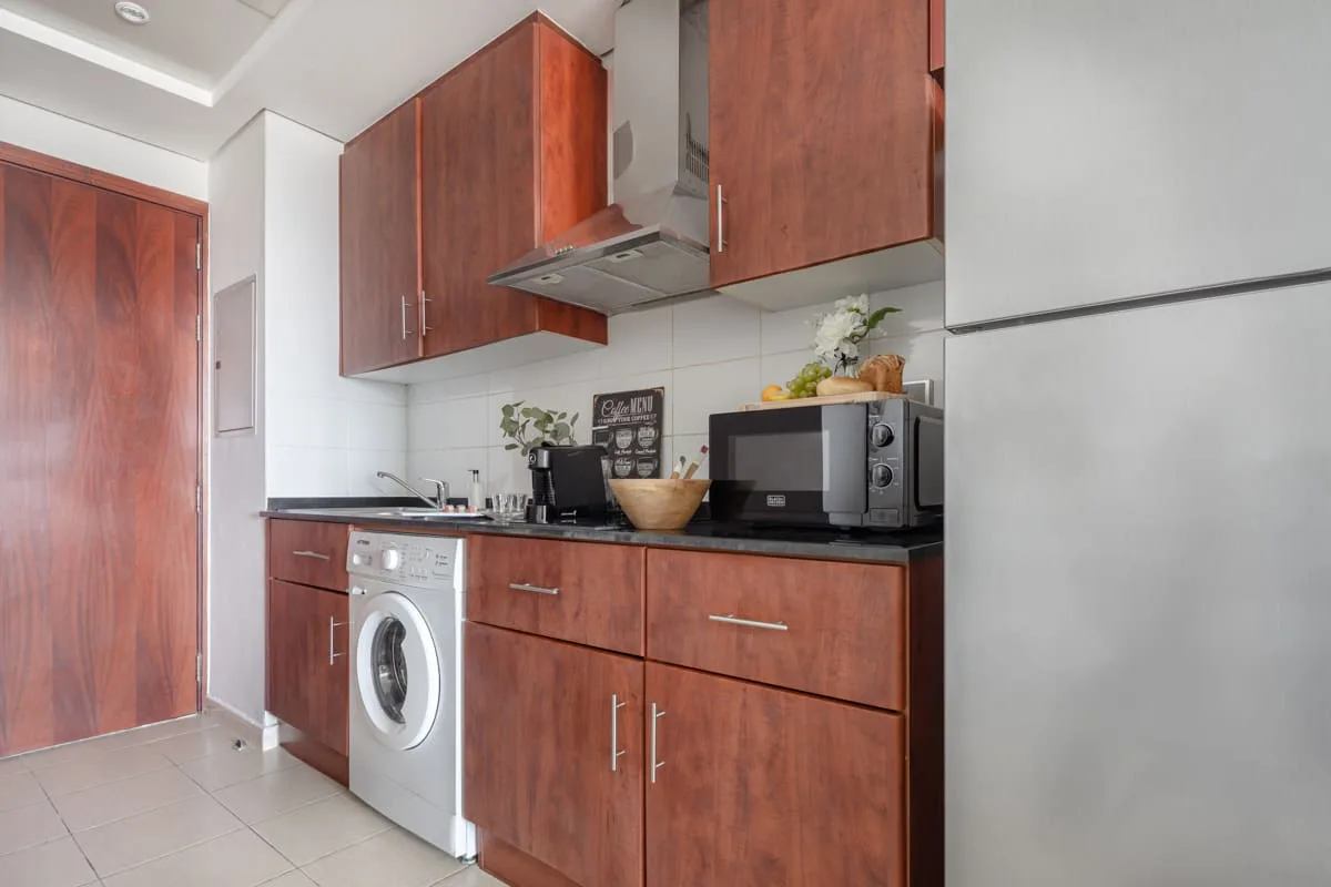 Una cocina compacta con gabinetes de madera rojiza, una encimera y una lavadora.