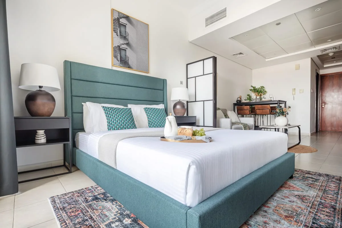 Dormitorio con una cama tapizada en turquesa y una pequeña zona de estar.