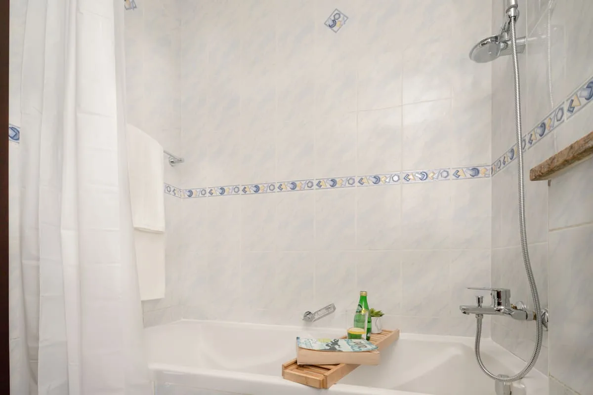 Un baño alicatado con bañera, ducha y una pequeña bandeja de madera.