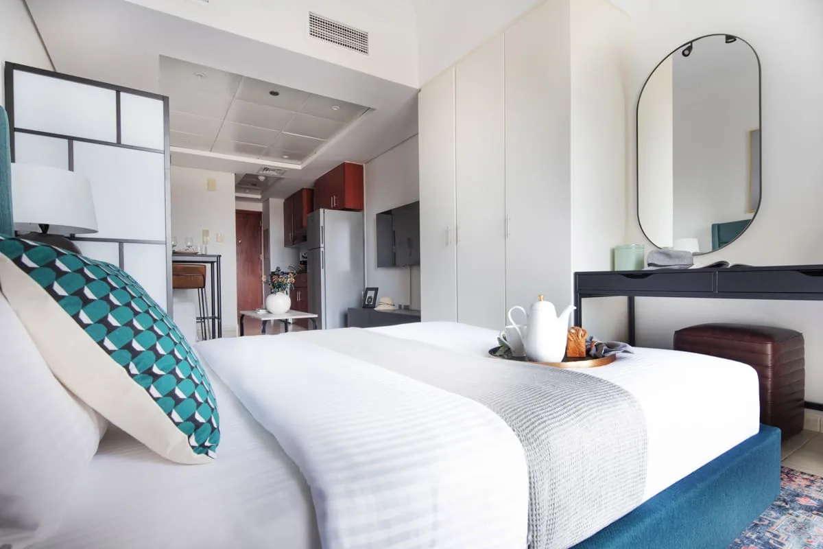 Un dormitorio luminoso con ropa de cama blanca y un espejo ovalado grande.