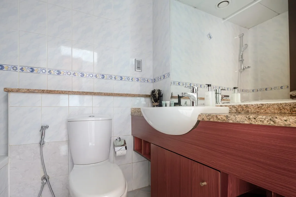 Un baño alicatado con inodoro, ducha higiénica y lavabo con mueble.
