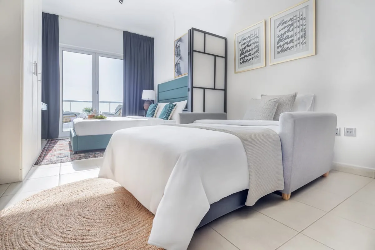 Un dormitorio luminoso con dos camas, cortinas oscuras y cuadros enmarcados.