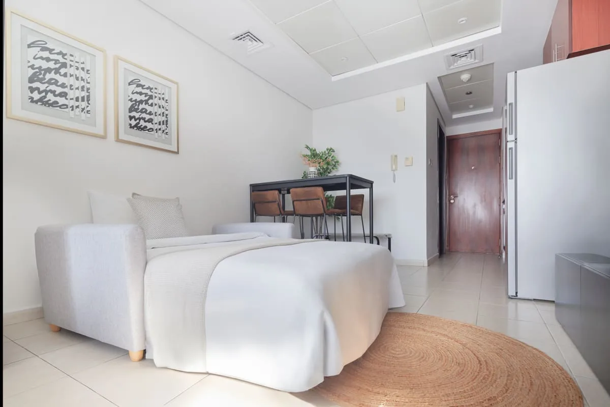 Una habitación luminosa con una cama, una mesa pequeña y una alfombra tejida.