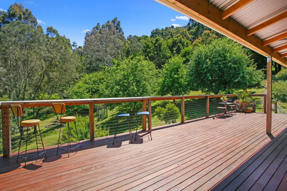 A covered outdoor deck with seating overlooks a green, wooded landscape.