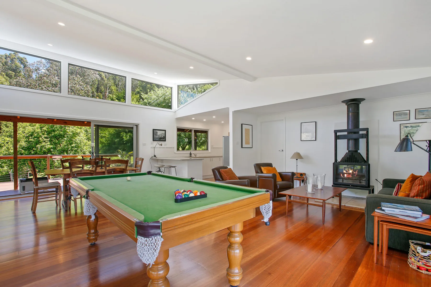 A bright living room with a pool table, seating, and large windows overlooking greenery.