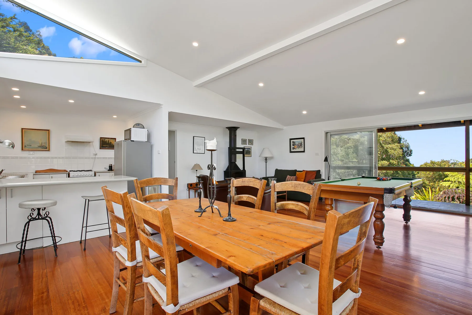 A bright open-plan dining and living area with wooden seating and a pool table.