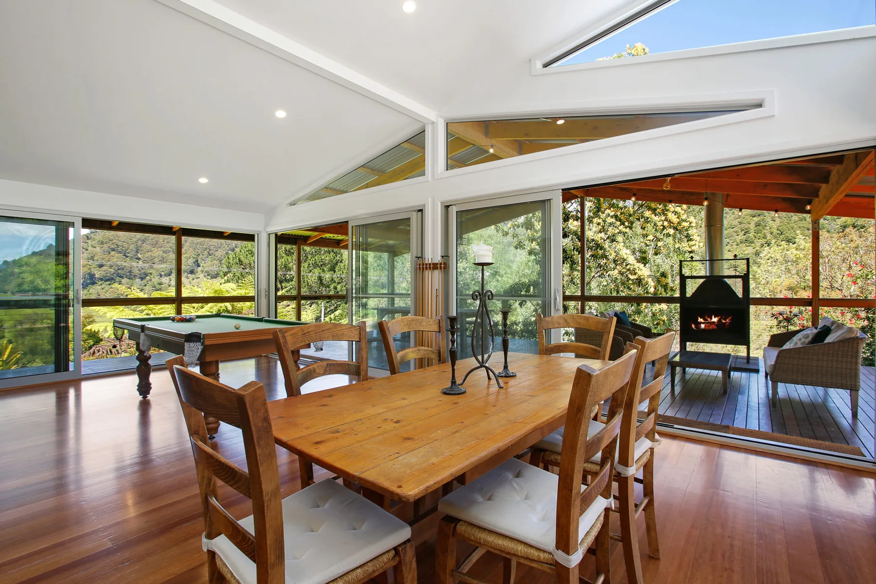 A dining area with wooden tables and chairs beside large windows opening onto a deck.