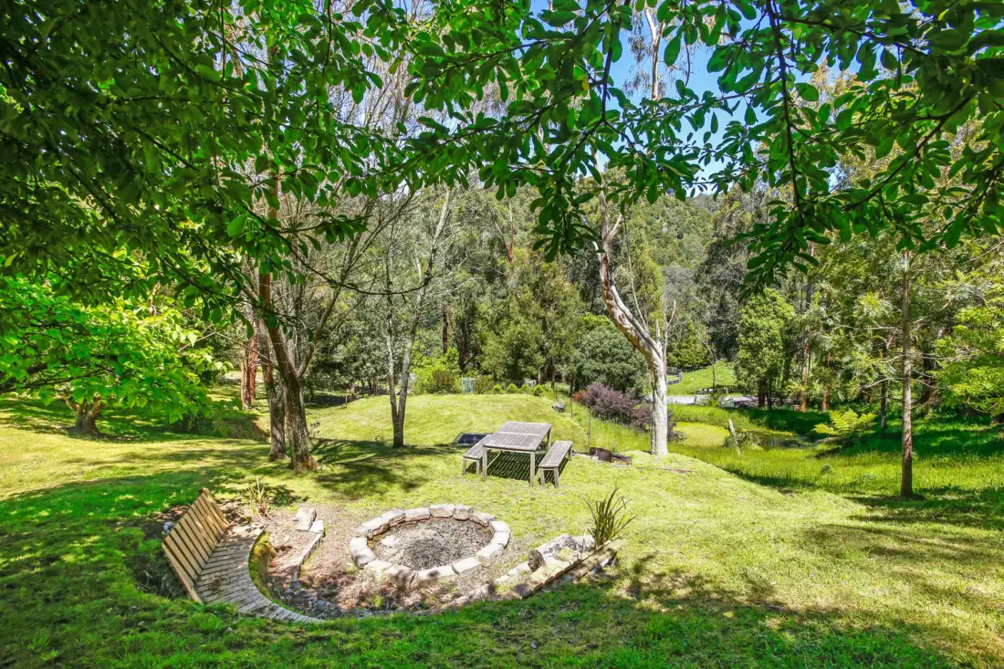A grassy garden with trees surrounds a stone fire pit and outdoor seating.