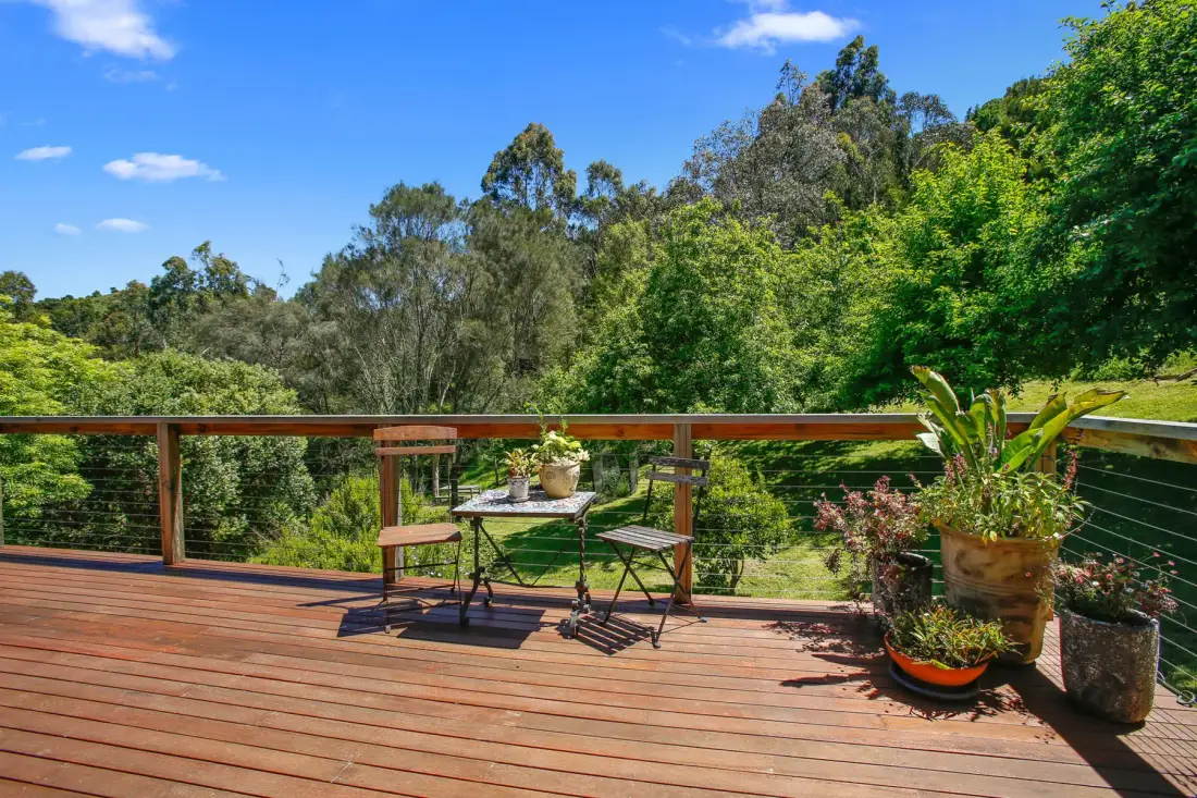 A wooden deck overlooks dense green trees beneath a clear blue sky.