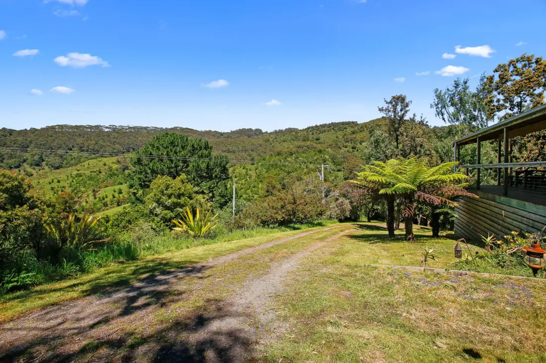 A grassy hillside overlooks a green valley, with a timber building at the edge.