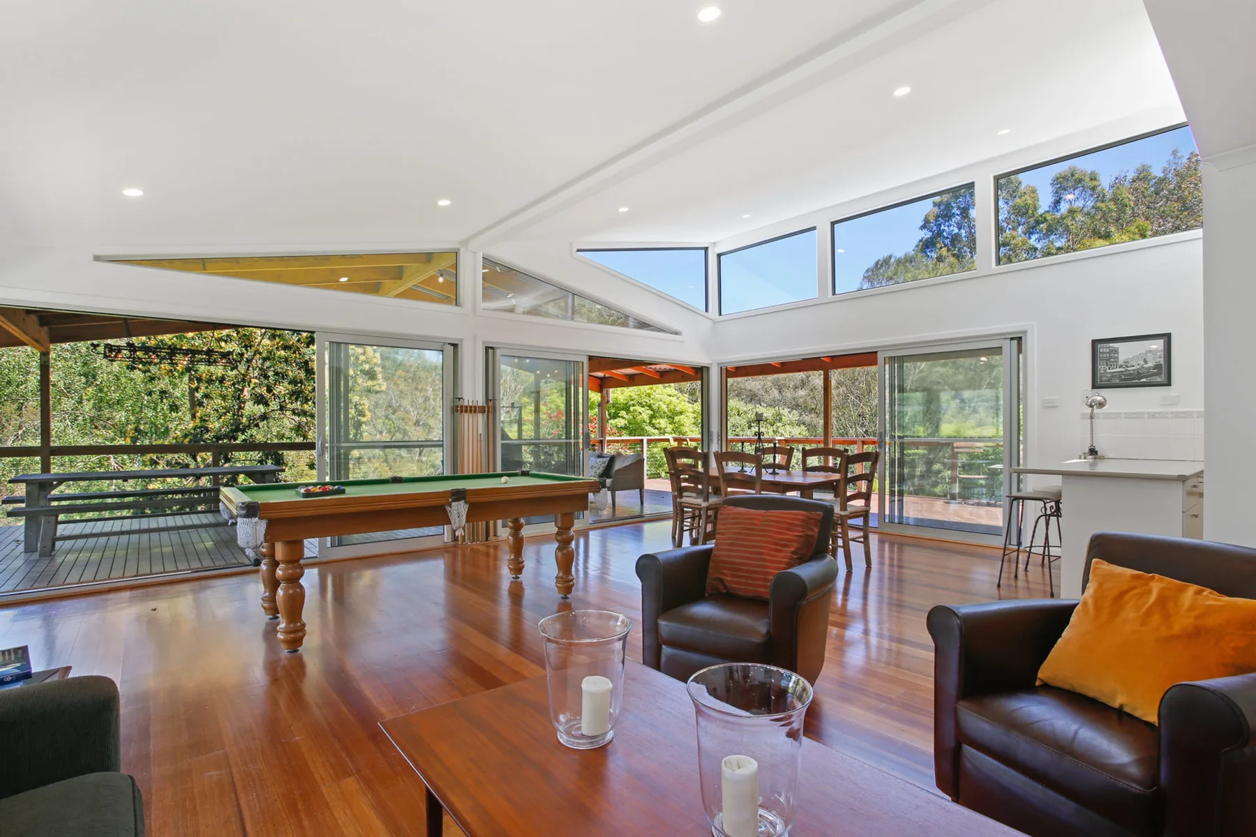 A bright living room opens onto a wooden deck through broad glass doors.