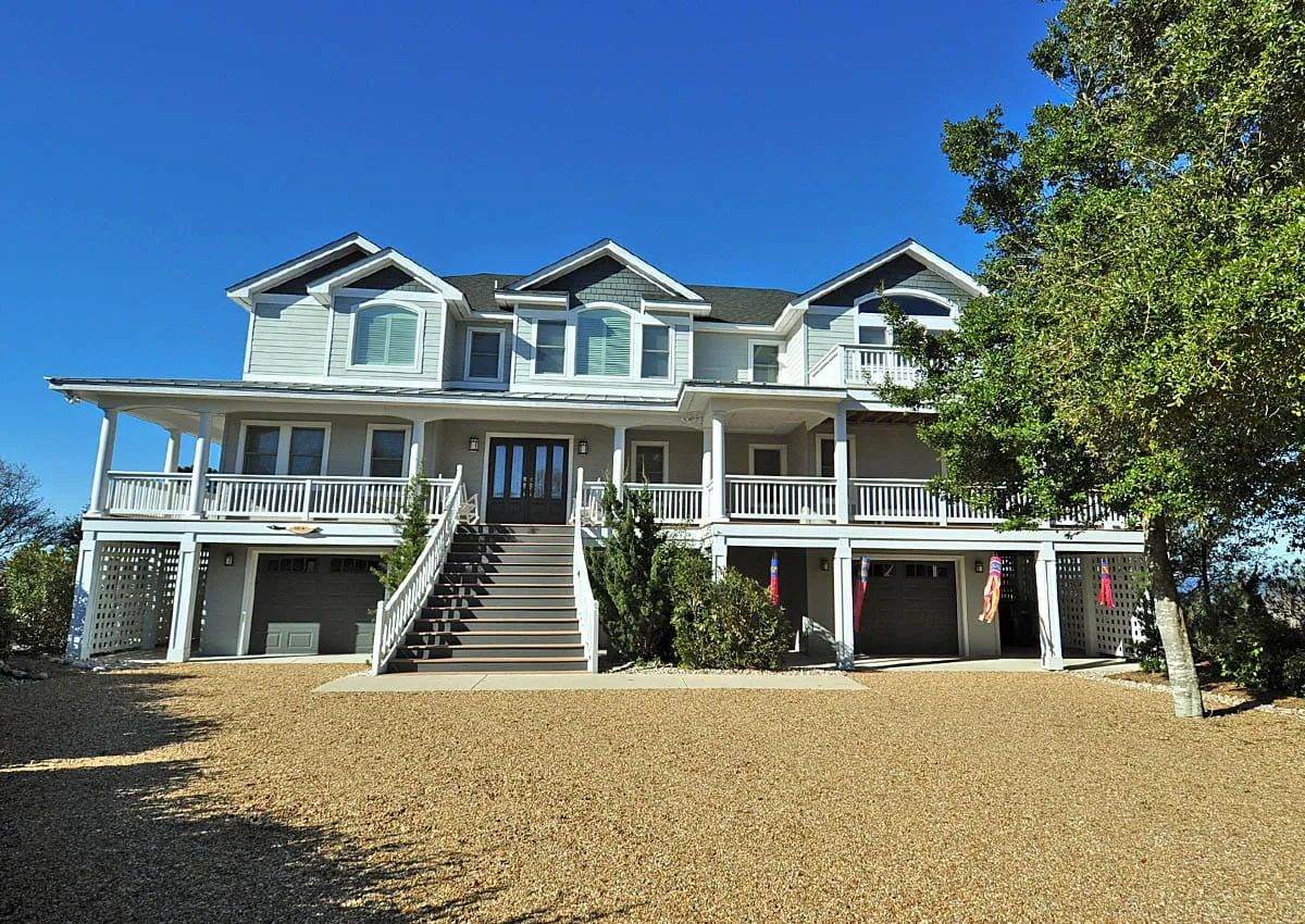 Una casa blanca grande con porches envolventes, escaleras exteriores y puertas de garaje.