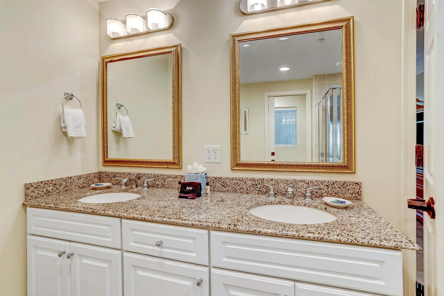A bathroom vanity with two sinks, mirrors, and wall-mounted lights.