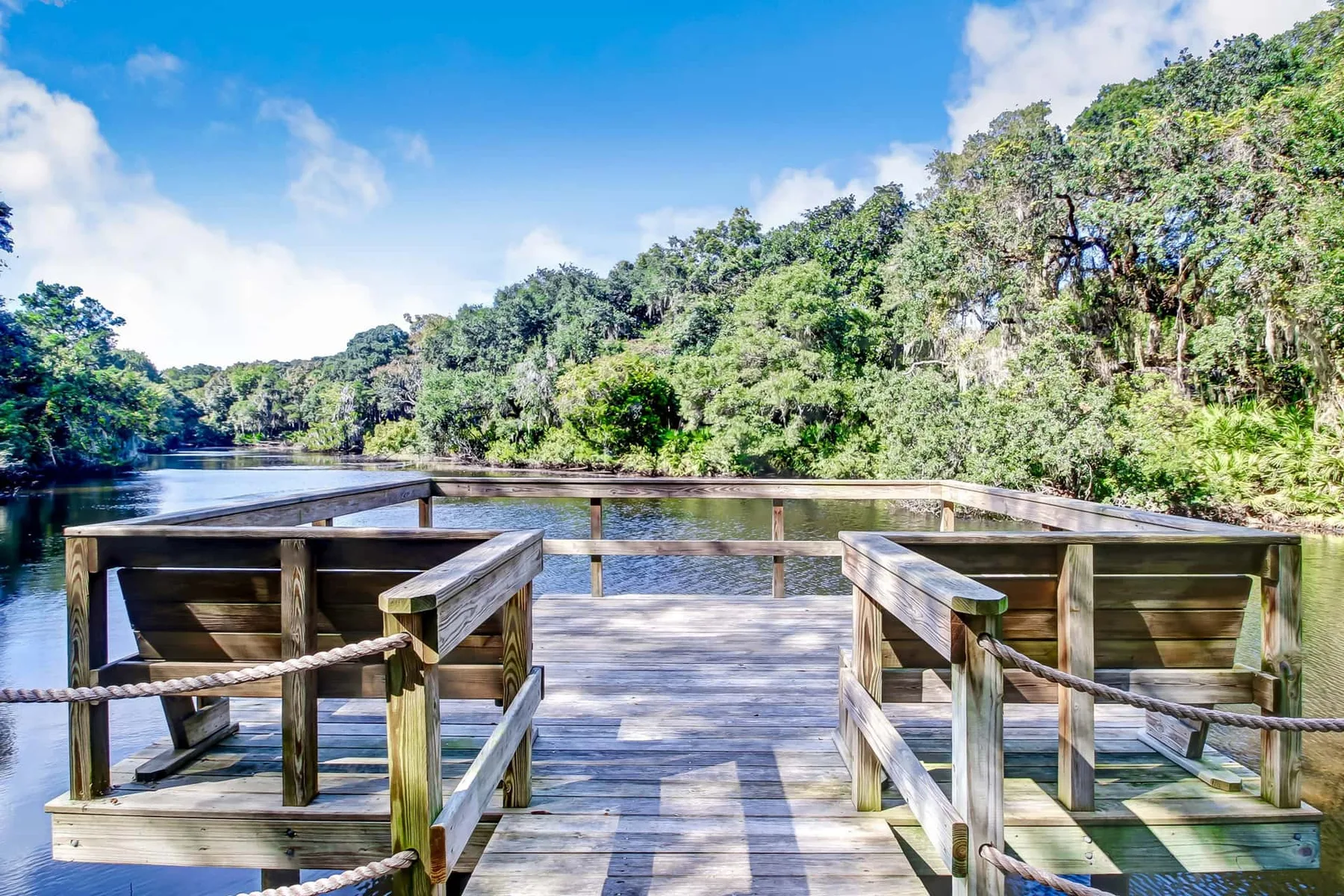 A wooden viewing deck extends over calm water beside a tree-lined shore.