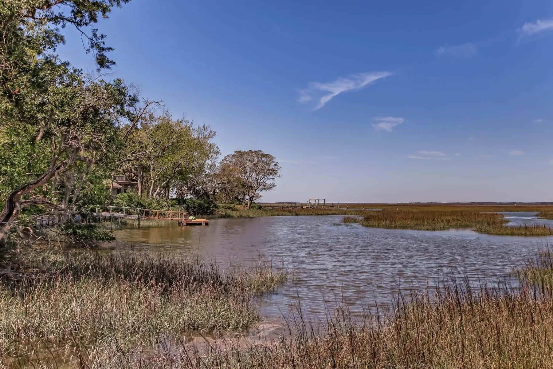 A marshland waterway stretches beneath a wide blue sky.