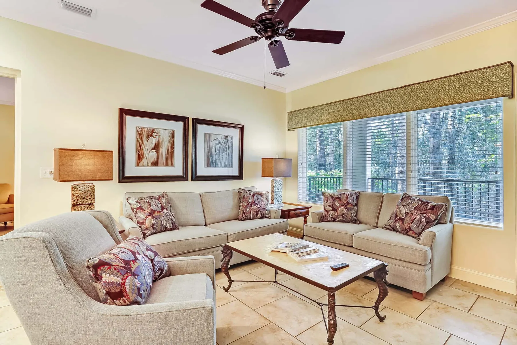 A bright living room with seating arranged around a coffee table beside large windows.