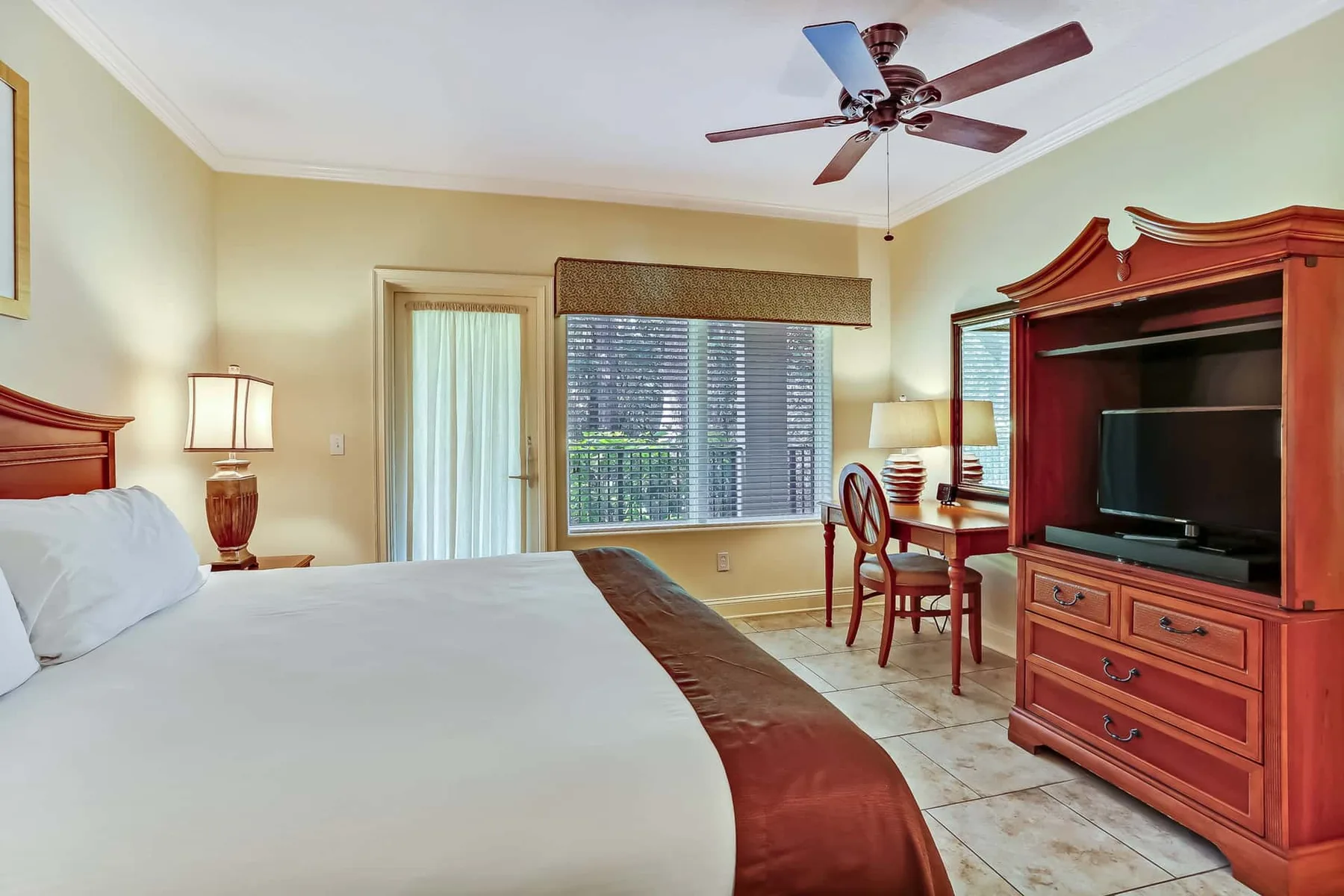 A bedroom with a bed, ceiling fan, and wooden entertainment cabinet.