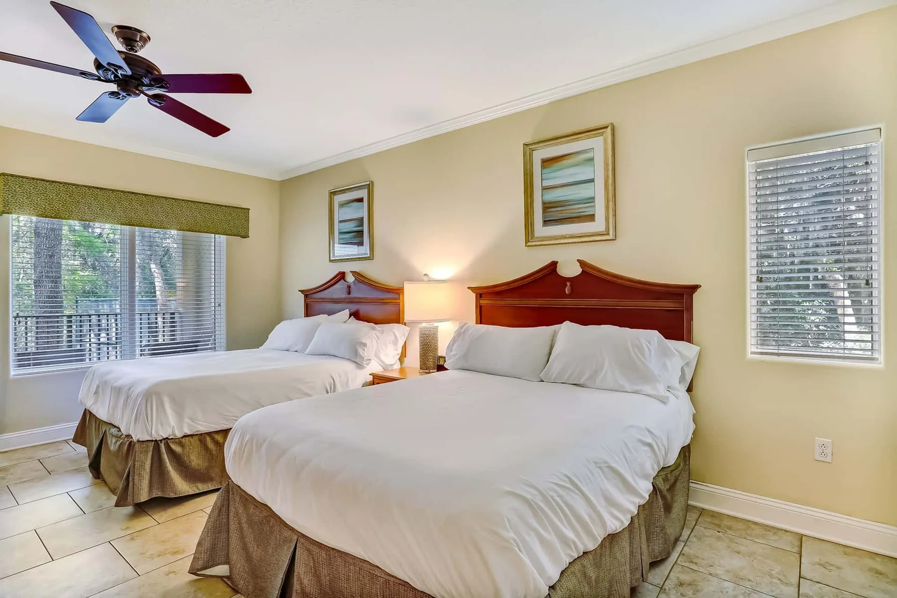 A bedroom with two beds, white bedding, and windows with blinds.