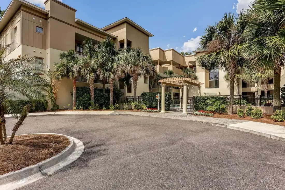 A tan multi-story building stands behind a paved driveway and palm trees.