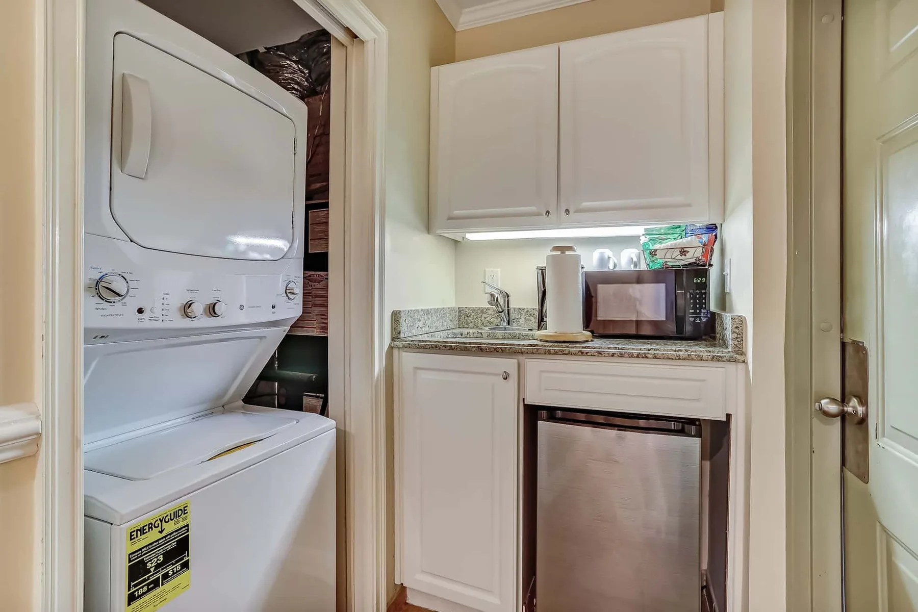 A laundry area with stacked appliances beside white cabinets and a counter.