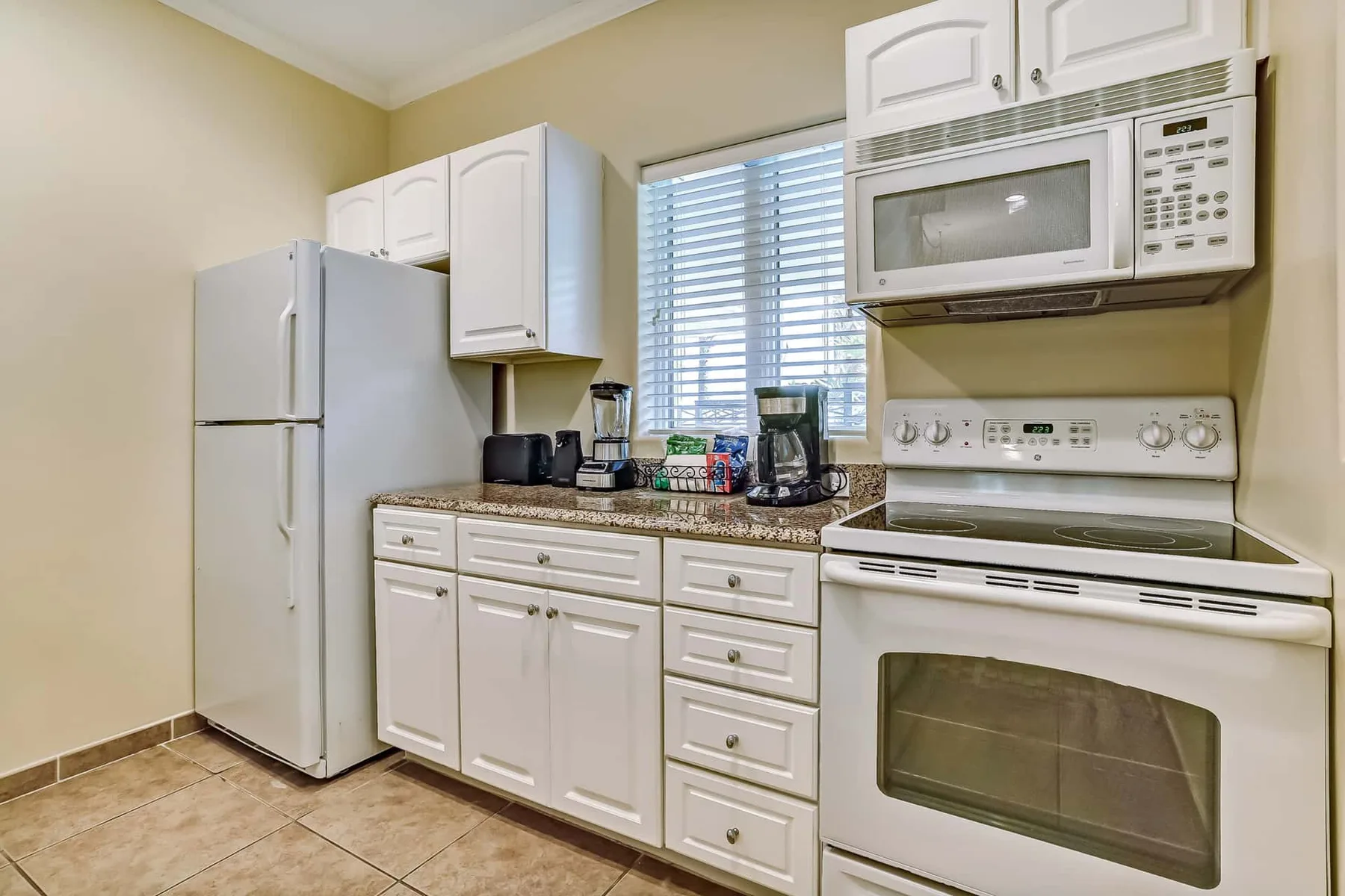 A bright kitchen with white cabinets, a refrigerator, and an electric range.