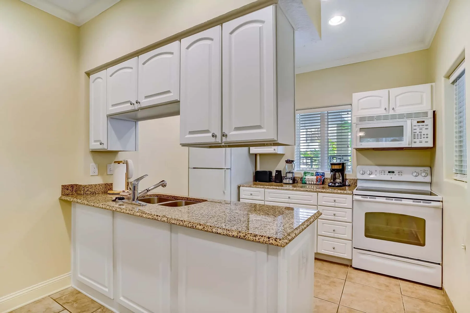 A bright kitchen with white cabinetry, a counter, and cooking appliances.