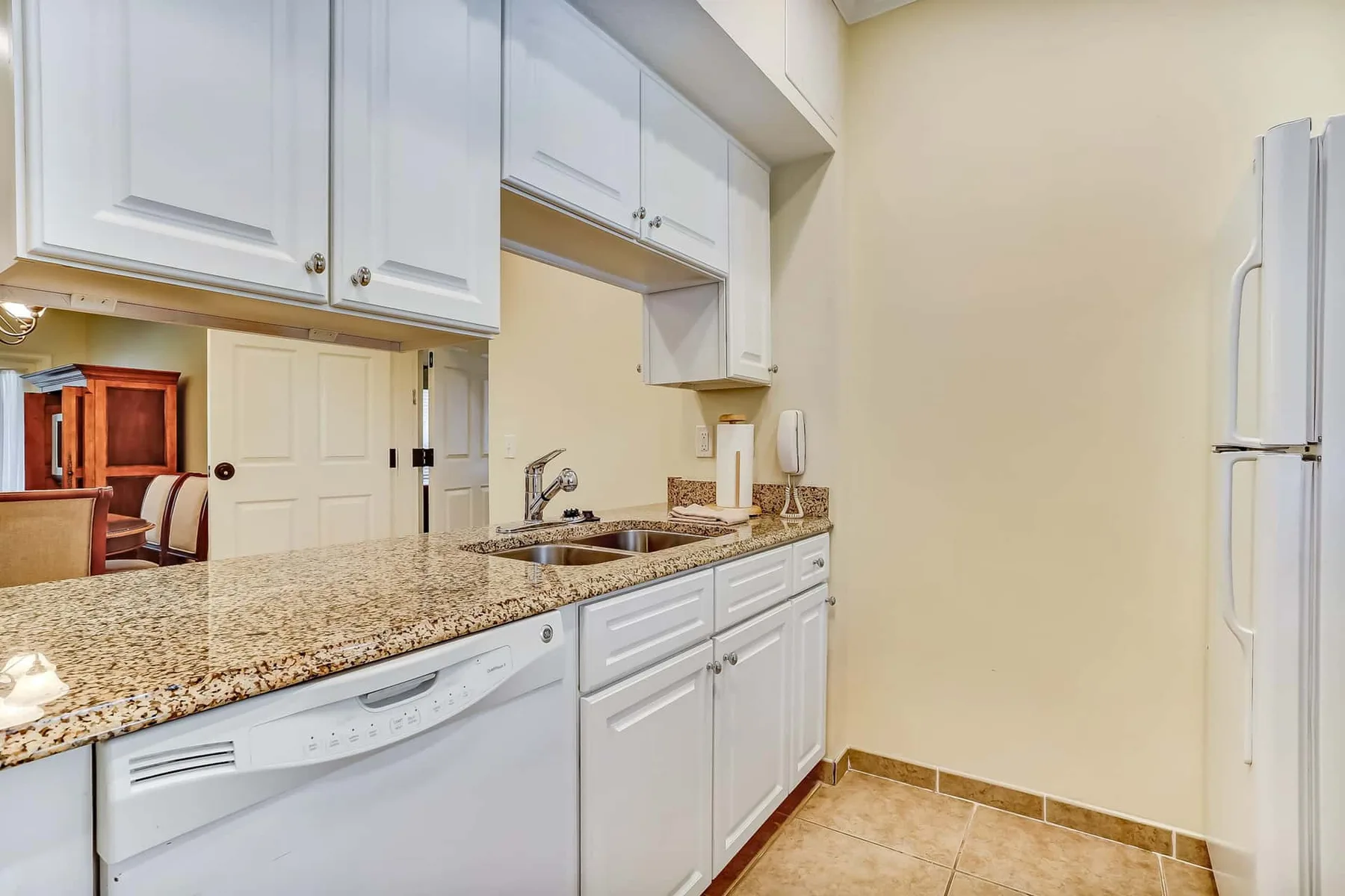 A bright kitchen with white cabinets, a counter, and a refrigerator.