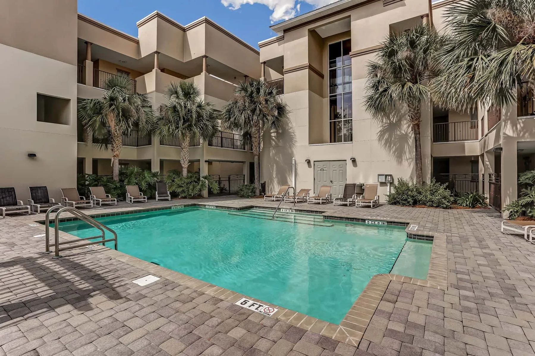 An outdoor swimming pool is surrounded by lounge seating and a multi-story building.