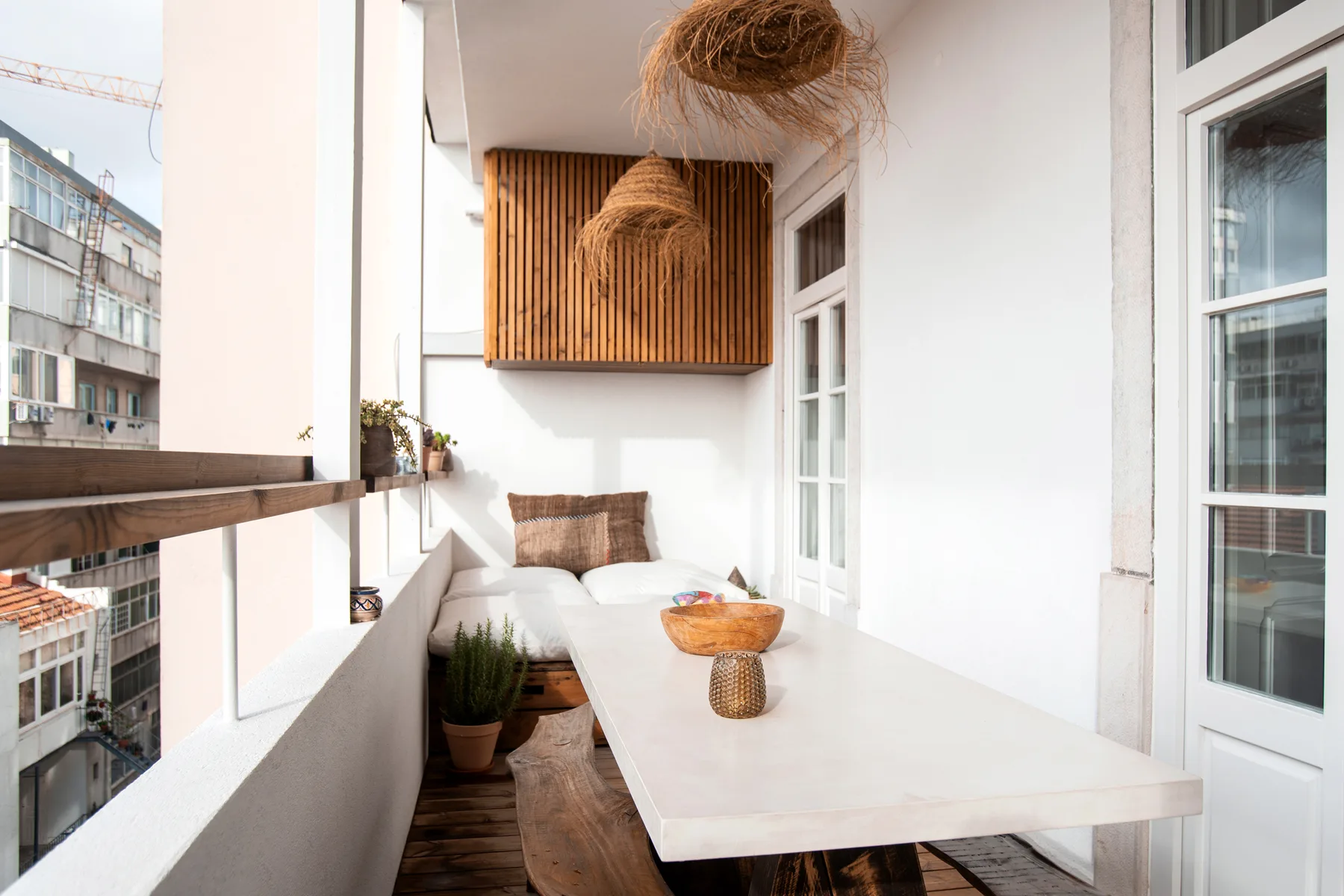 A bright balcony dining area with a long table and woven pendant lights.