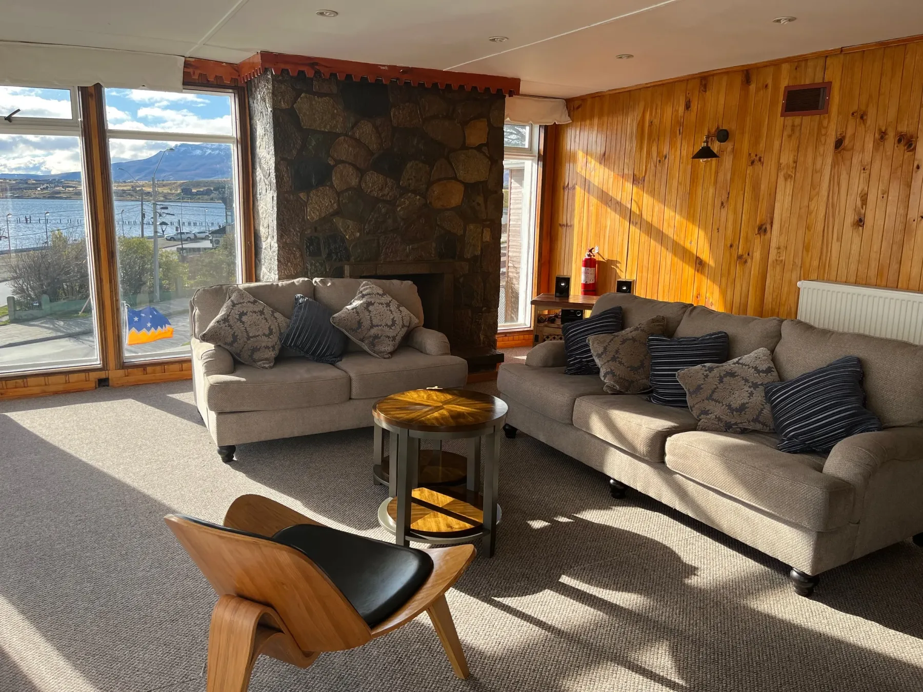 Sala de estar con sillones, chimenea de piedra y ventanas hacia el fiordo