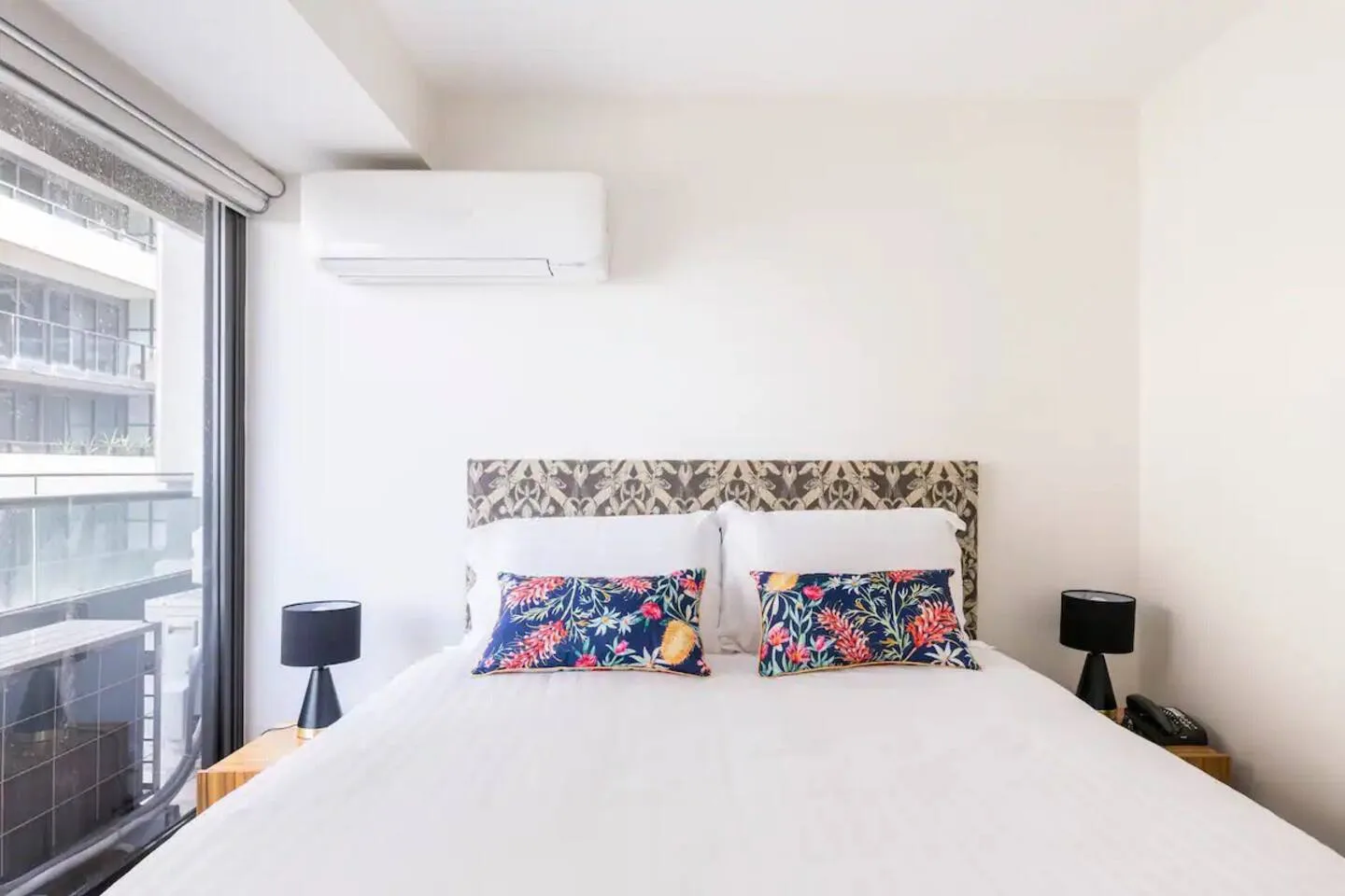 A bright bedroom with a bed, patterned headboard, and large window.