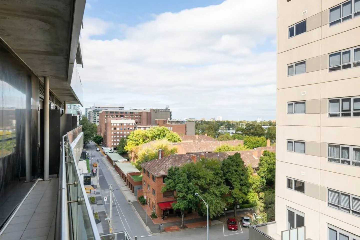 A balcony overlooks nearby buildings, trees, and a street.