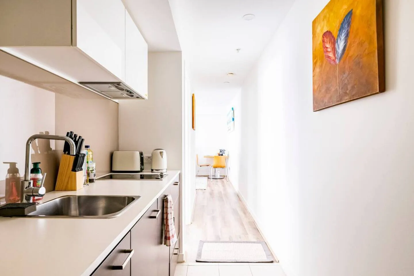 A compact kitchenette with a sink and countertop opens onto a bright hallway.