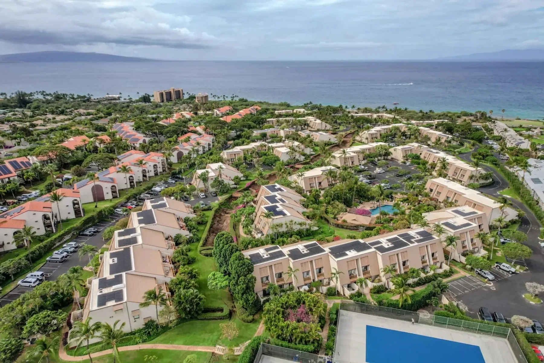 Vista aérea de un complejo residencial costero con jardines y el océano al fondo.