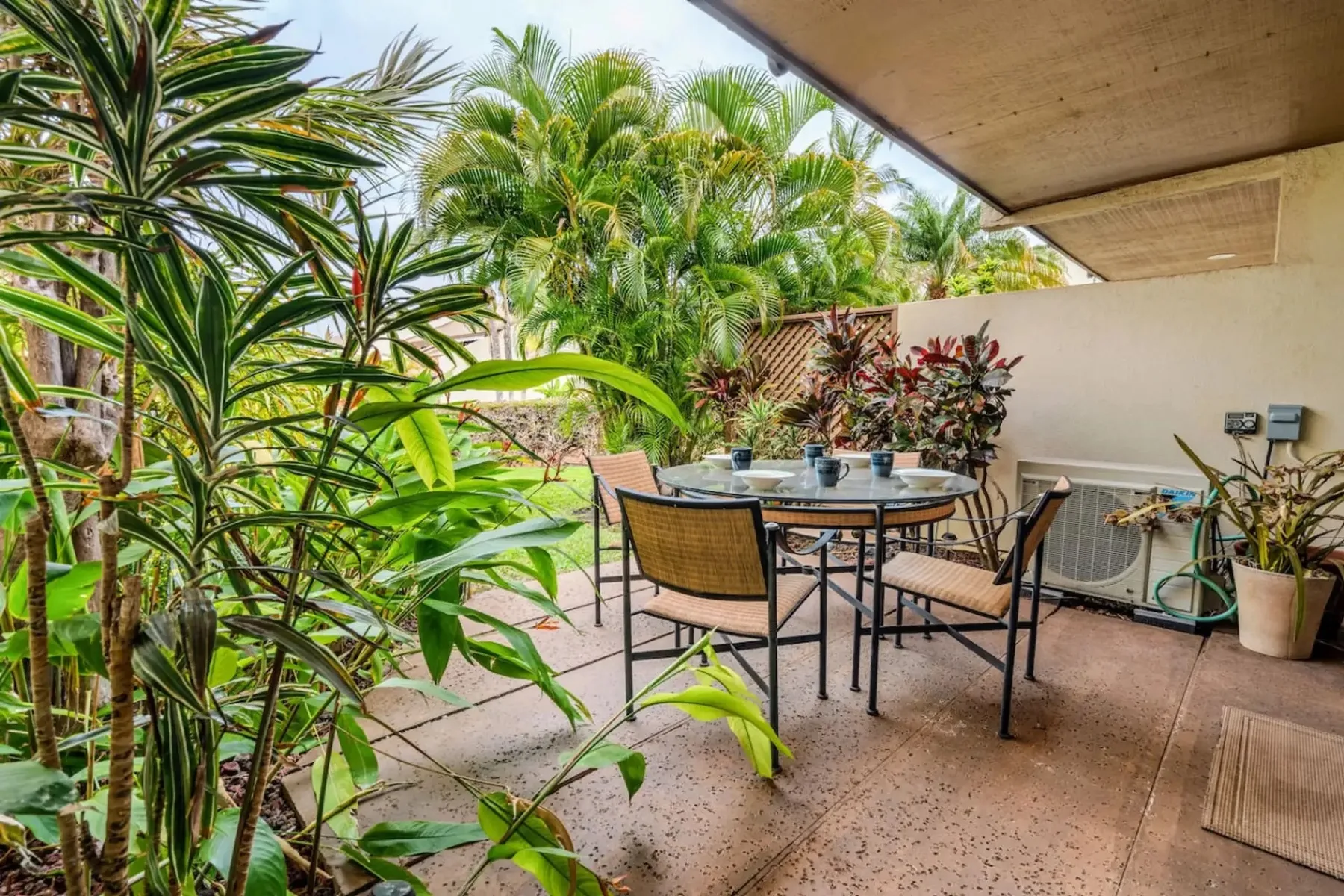 Un patio cubierto con una mesa de comedor y sillas, rodeado de plantas tropicales.