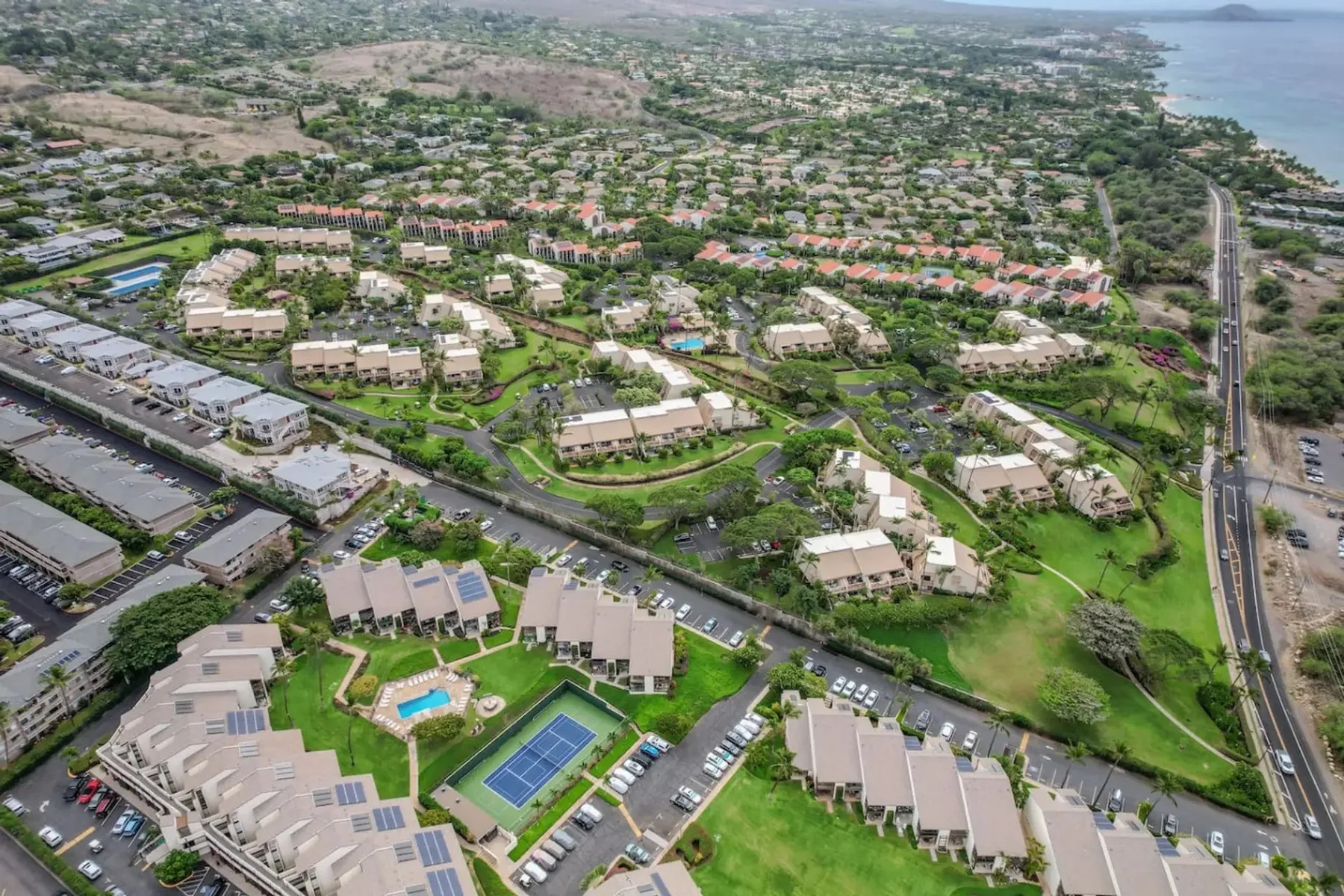 Vista aérea de una comunidad residencial con zonas verdes y una pista deportiva.