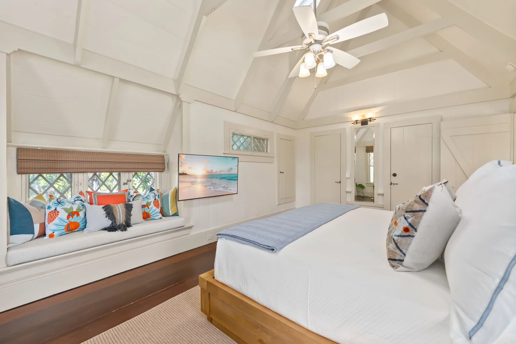 Un dormitorio luminoso con una cama y un asiento junto a la ventana con cojines coloridos.