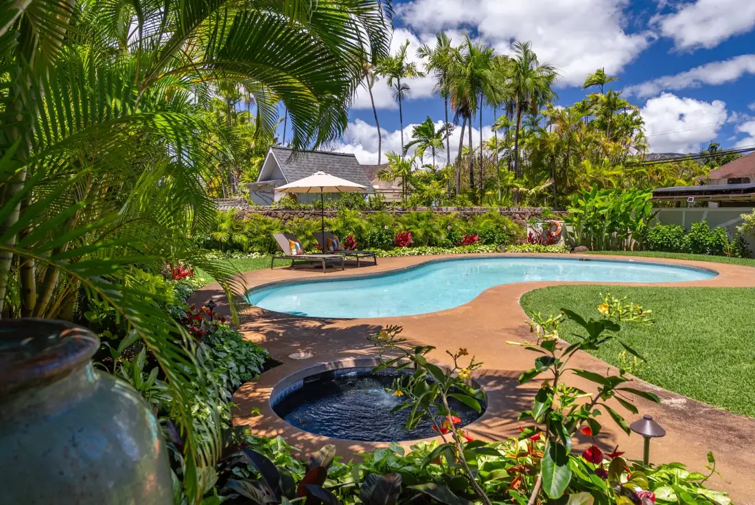 Una piscina al aire libre ajardinada está rodeada de plantas tropicales y palmeras.