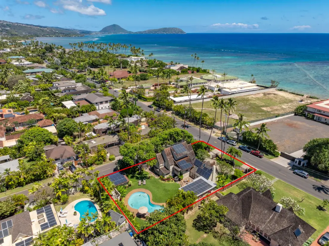 Vista aérea de un barrio costero con una propiedad señalada y piscinas.