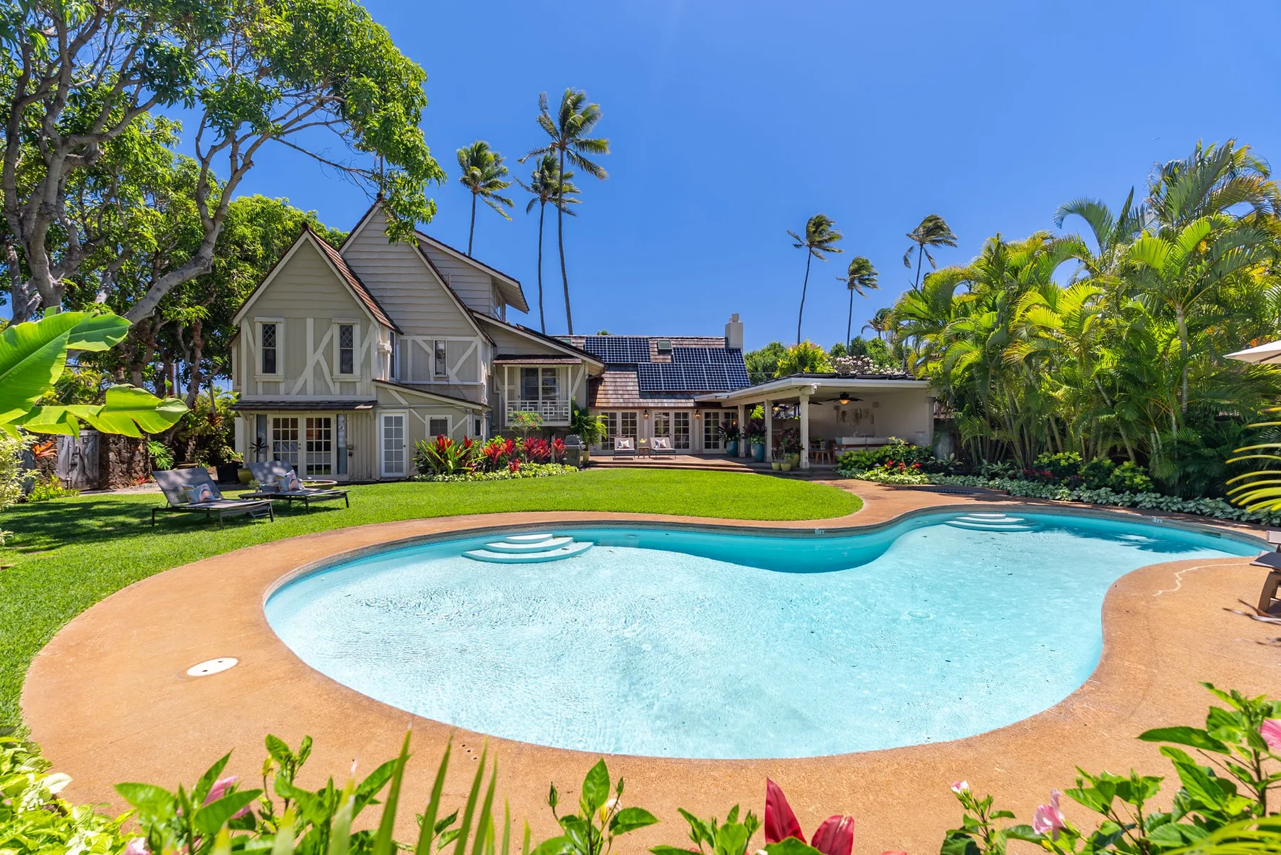 Una piscina de forma curva está en un jardín junto a una casa.